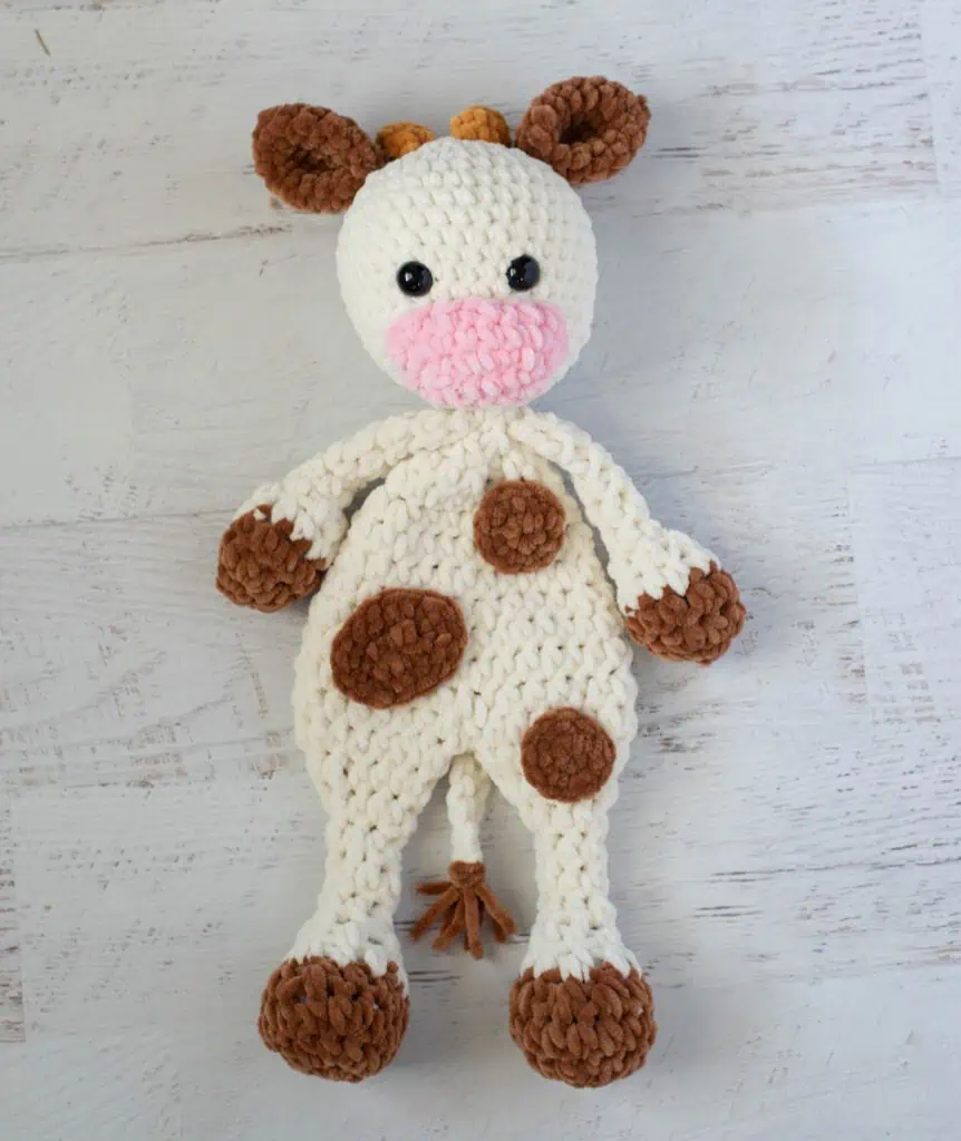 crochet cow snuggler made in cream, brown and pink chenille yarn.