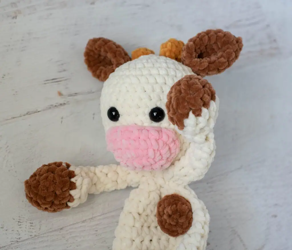 crochet cow snuggler made in cream, brown and pink chenille yarn.
