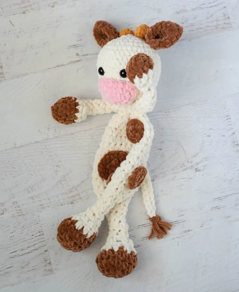crochet cow snuggler made in cream, brown and pink chenille yarn.