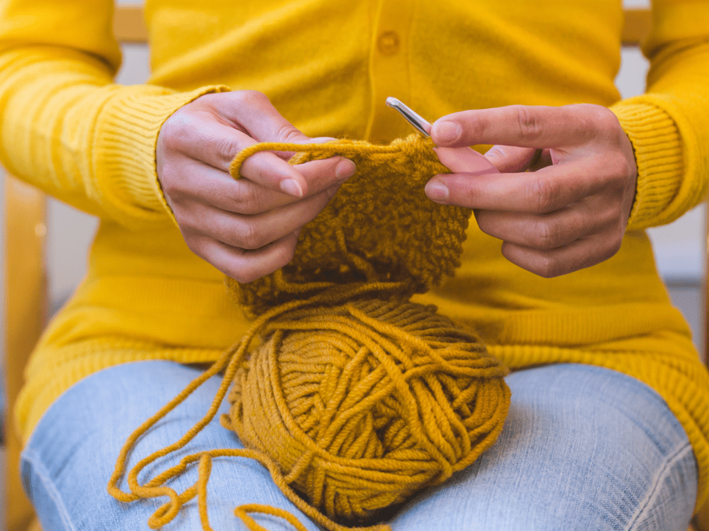 Woman in yellow sweater and jeans crocheting with yellow yarn