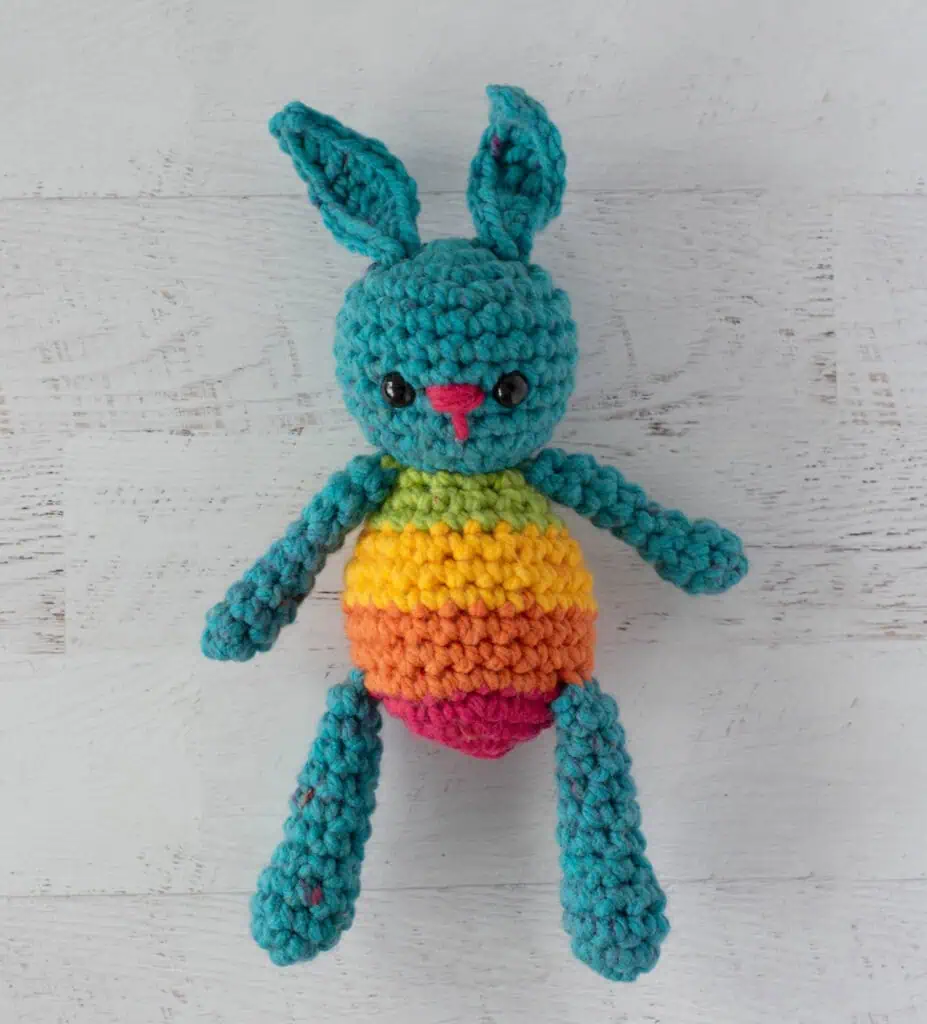 Blue crochet bunny with a rainbow striped body laying