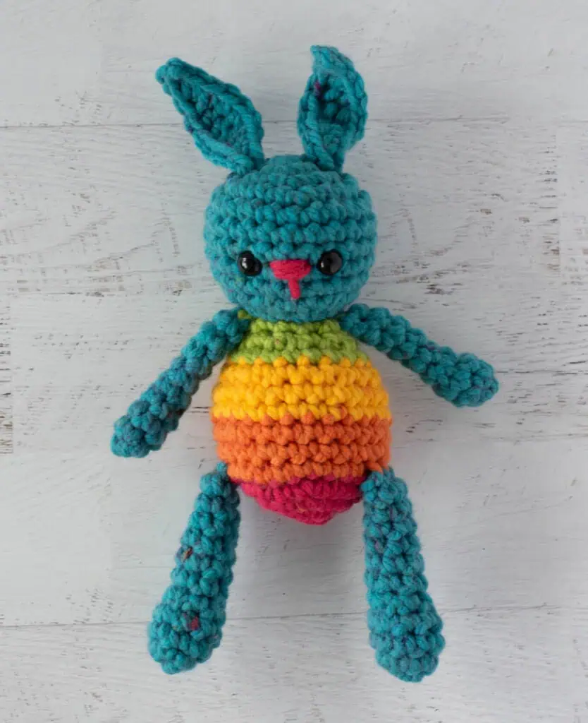 Blue crochet bunny with a rainbow striped body laying