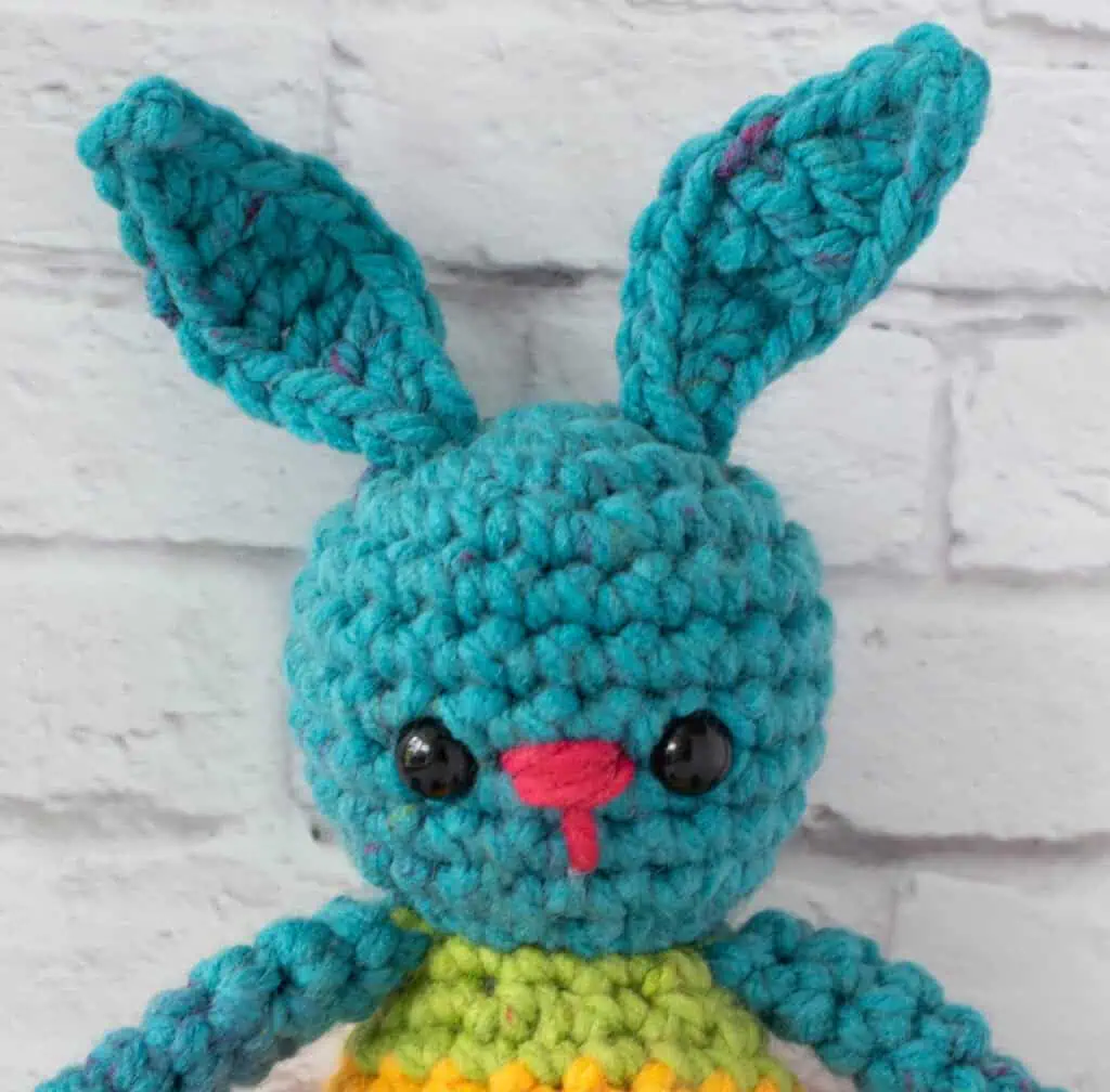 Close up of Crochet bunny face with blue, reddish pink and green yarn