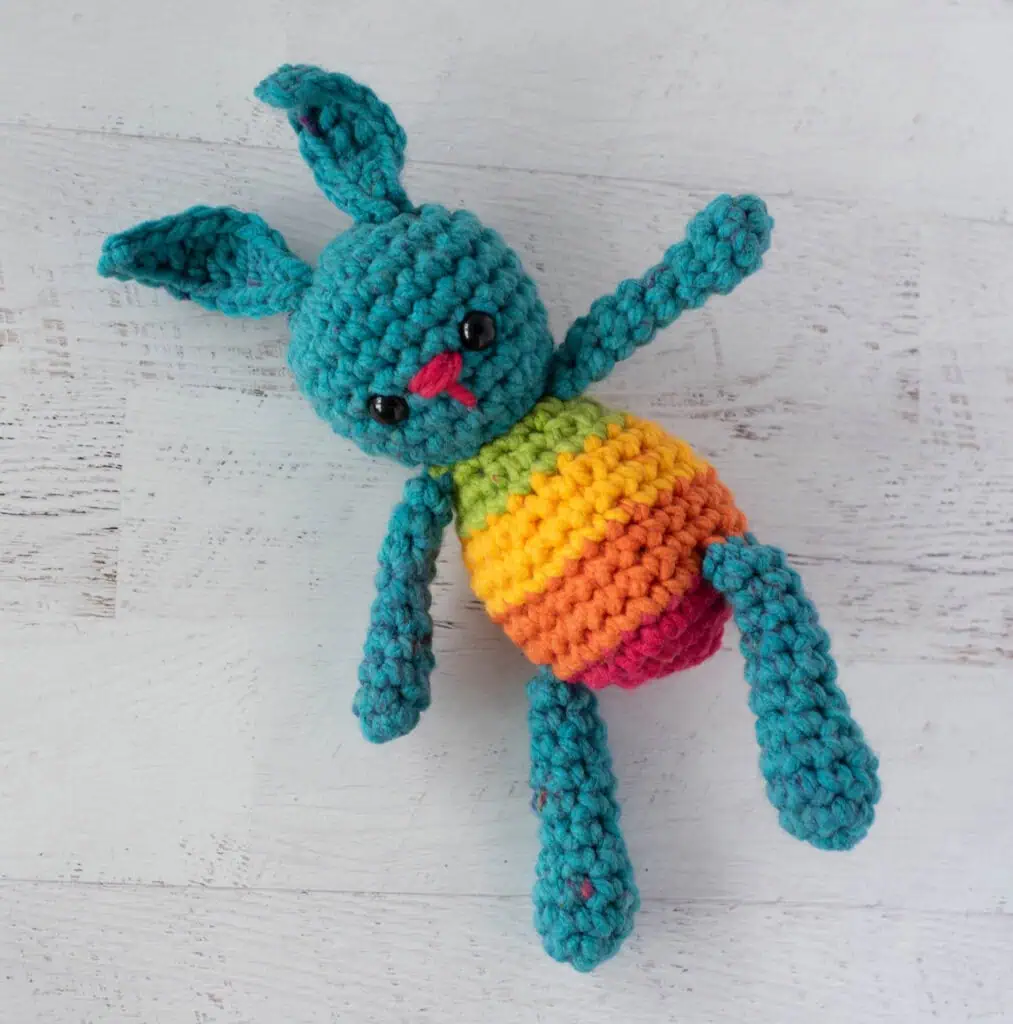 Blue crochet bunny with a rainbow striped body laying