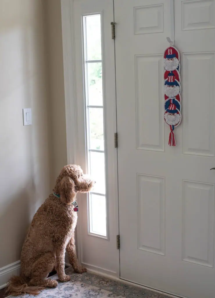 Crochet Uncle Sam Wallhanging in Red, White and Blue Yarn on white door with dog sitting looking out a side window