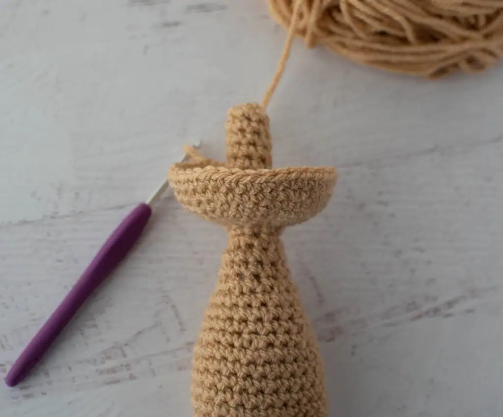 Crochet doll body, neck and head in progress construction with beige yarn.