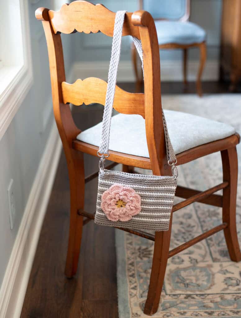 Gray crochet bag with white stripes and pink flower on a chair