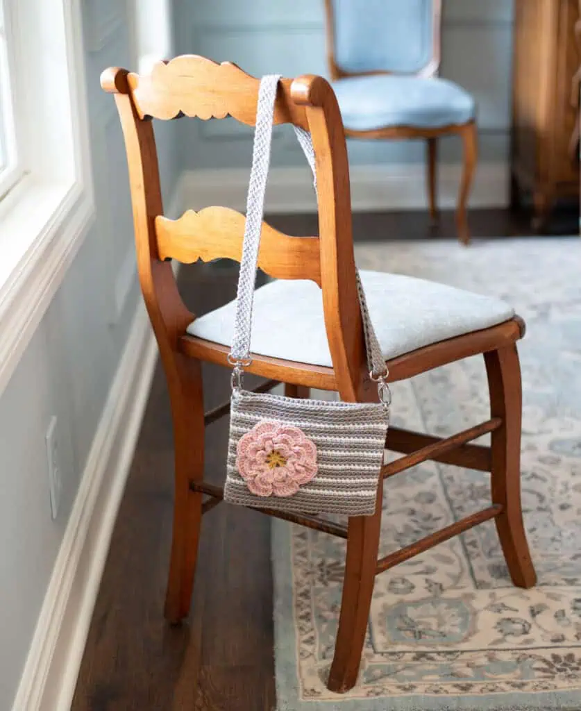 Gray crochet bag with white stripes and pink flower on a chair