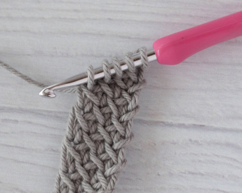 crochet strap in gray yarn with a pink crochet hook