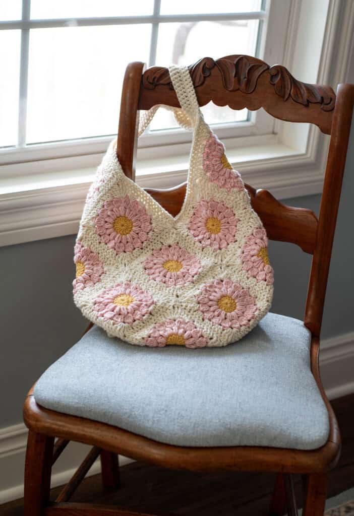 Pink and yellow flower granny square bag on blue chair next to window