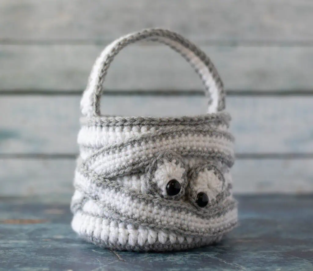 crochet halloween bag in gray and white with straps wrapping bag and eyeballs to look like a crochet mummy.