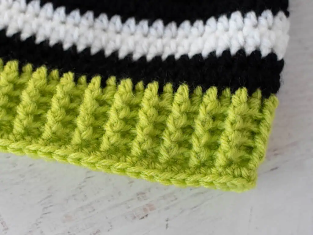 Edge of crochet hat in green yarn with black and white stripes