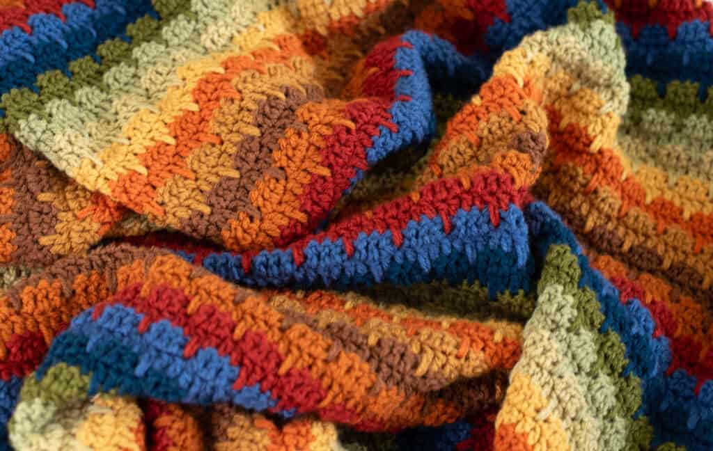 Crochet scrap afghan in multiple shades of green, orange, brown, red, blue and yellow yarn