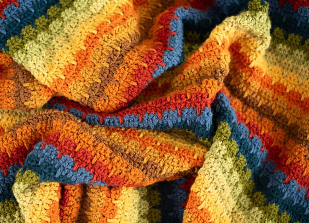 Crochet scrap afghan in multiple shades of green, orange, brown, red, blue and yellow yarn