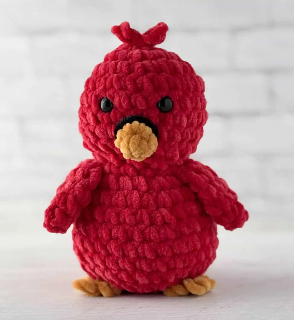 Crocheted bird in red with gold beak and feet and black eyes and ring around beak