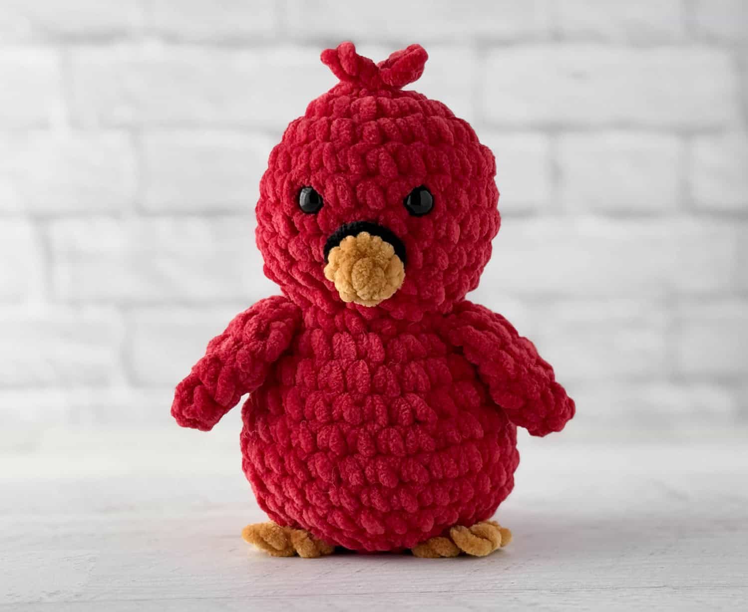 Crocheted bird in red with gold beak and feet and black eyes and ring around beak