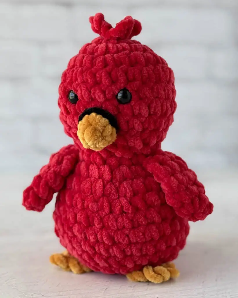Crocheted bird in red with gold beak and feet and black eyes and ring around beak