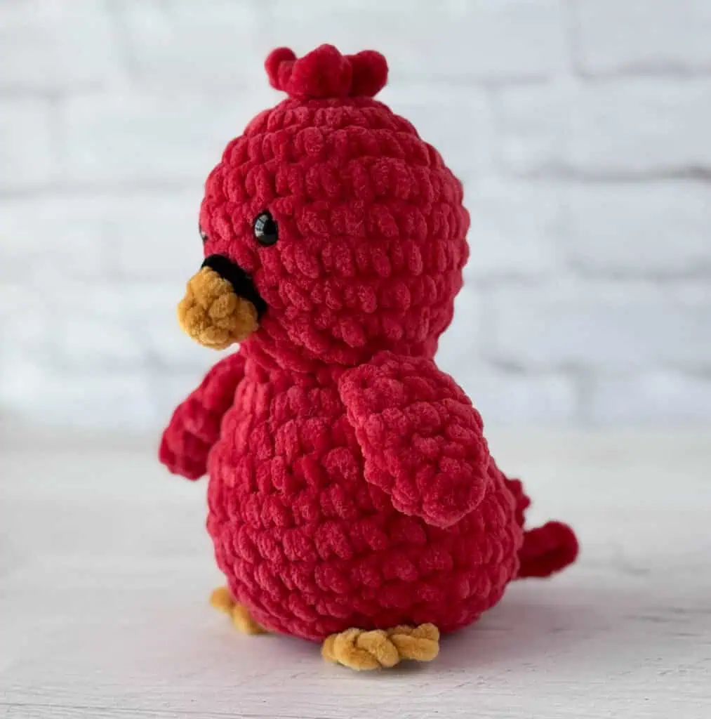 Crocheted bird in red with gold beak and feet and black eyes and ring around beak