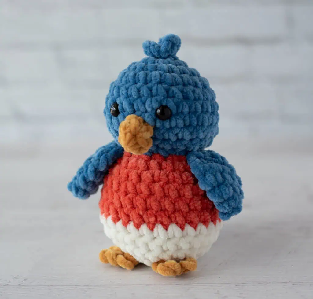 crochet bluebird out of plush blue, mango, cream and gold yarn