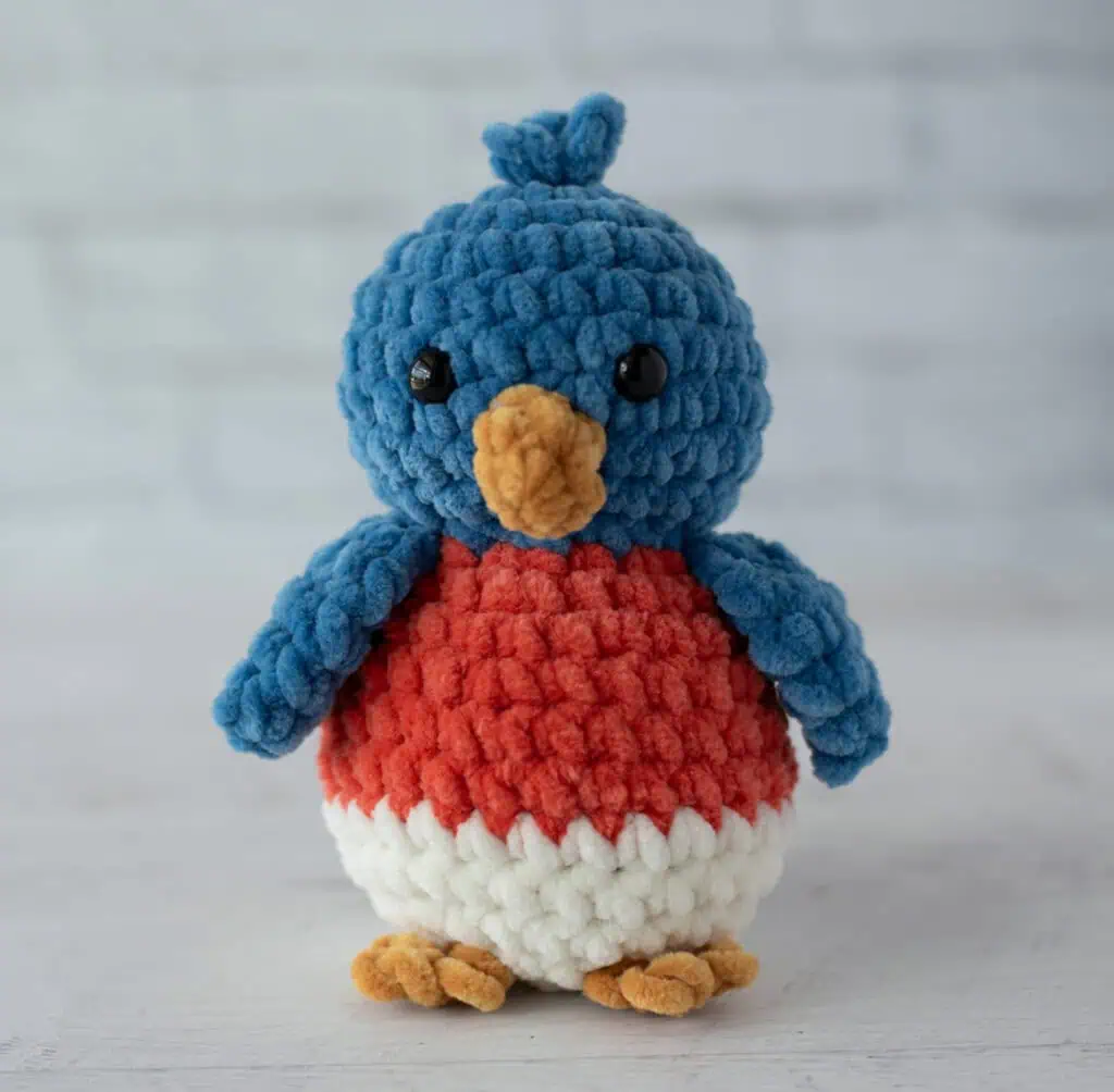 crochet bluebird out of plush blue, mango, cream and gold yarn
