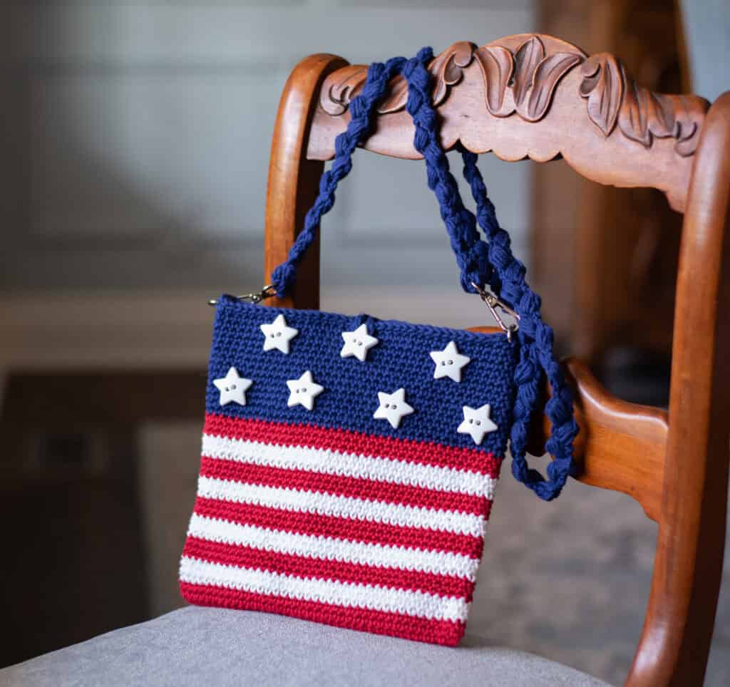 A crocheted purse with stars and stripes on a chair.