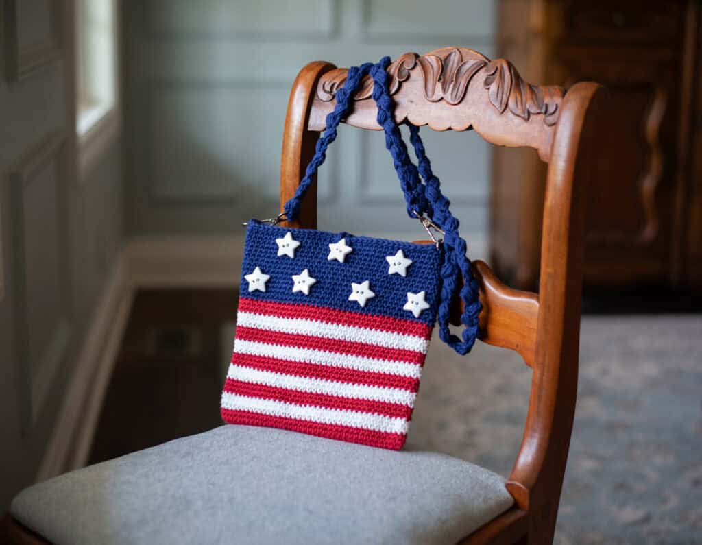A crocheted purse with stars and stripes on a chair.
