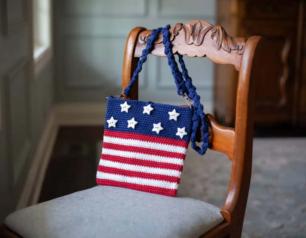 A crocheted purse with stars and stripes on a chair.