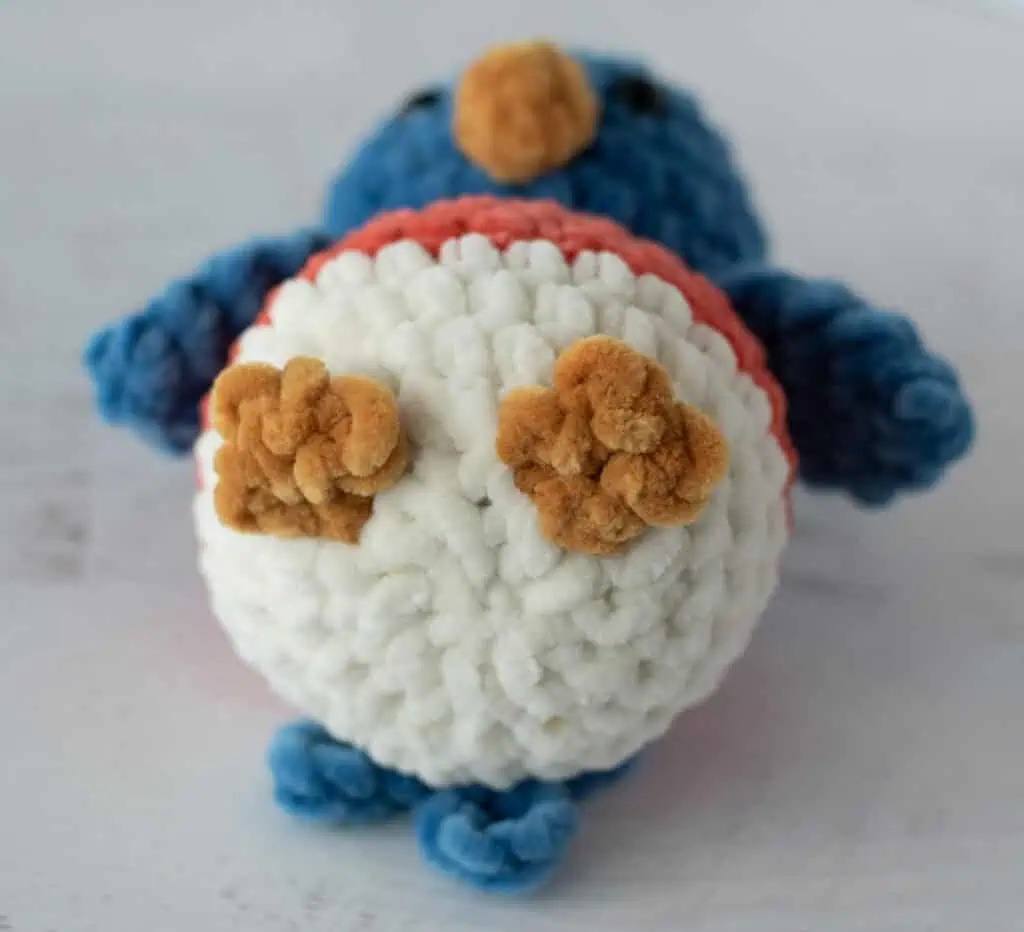 view of feet of crochet bluebird in gold and cream yarn