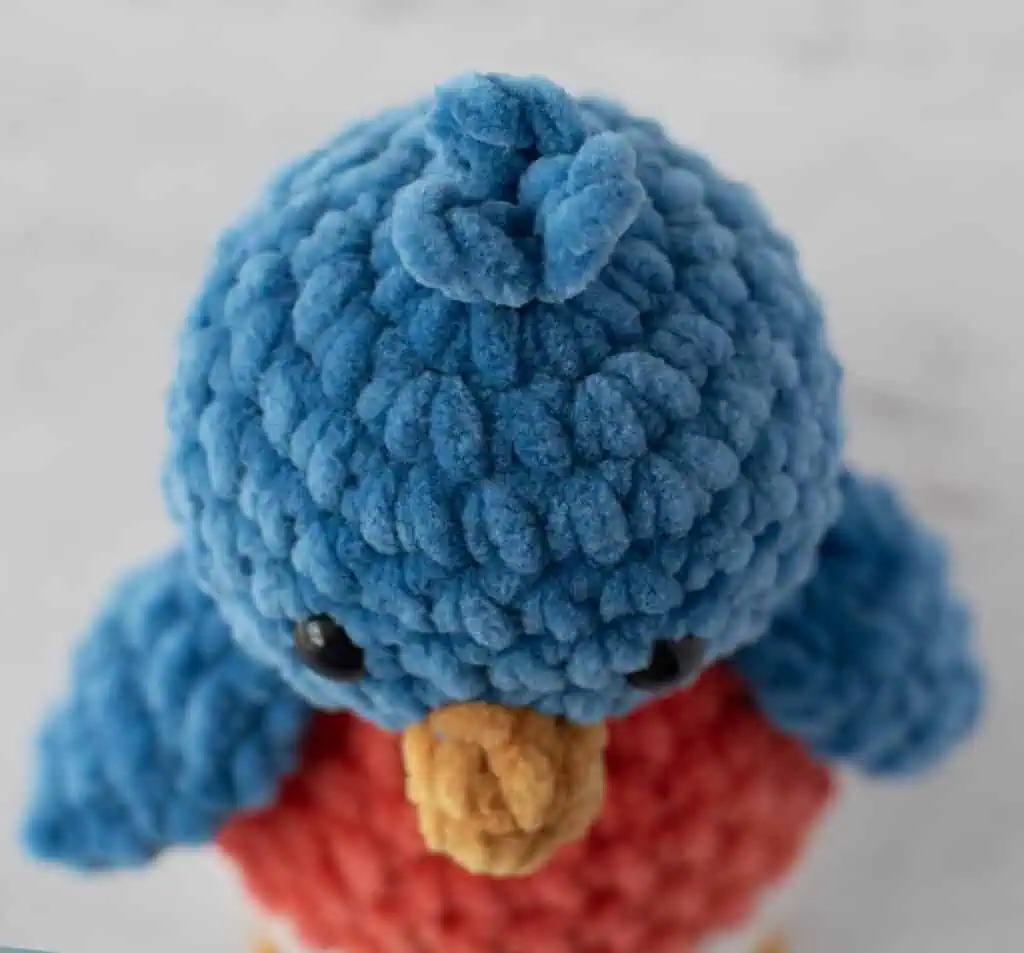 crochet bluebird top of head view, made out of plush blue, mango, cream and gold yarn