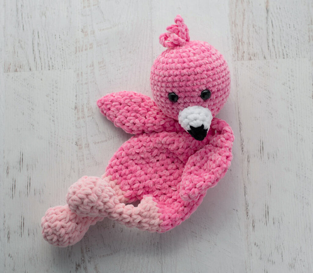 Crochet flamingo in pink yarn with a white and black beak laying on side