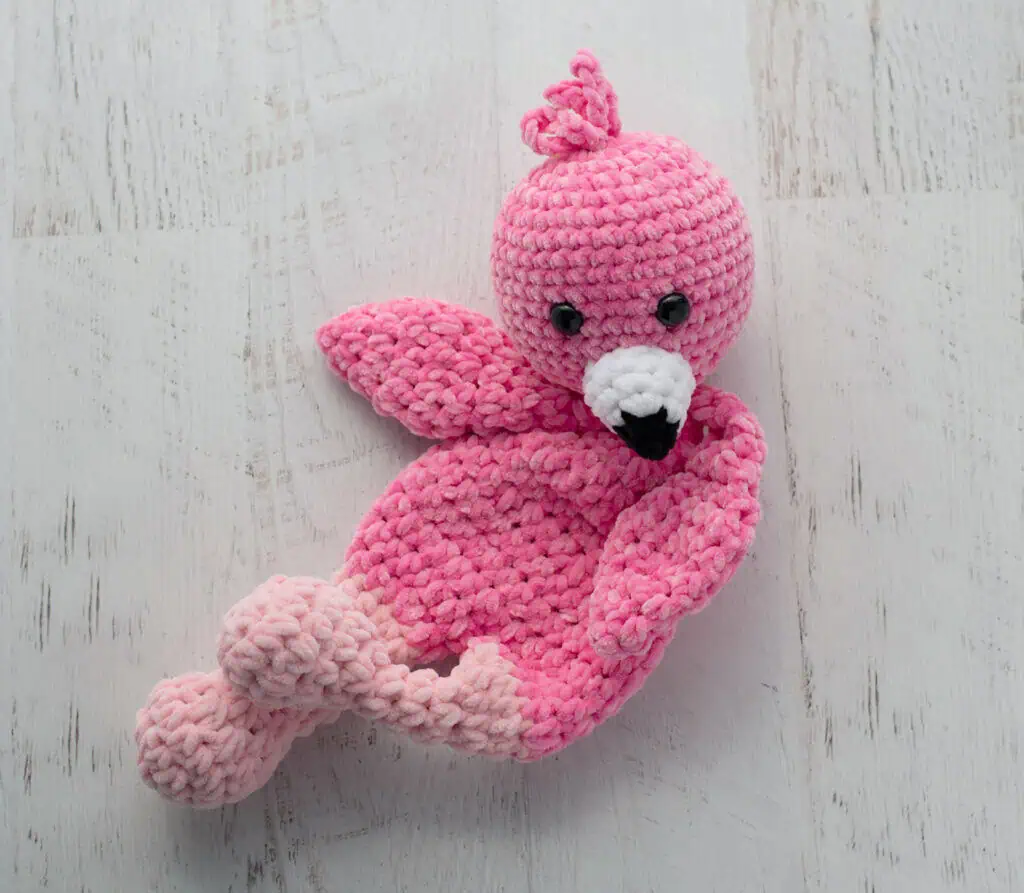 Crochet flamingo in pink yarn with a white and black beak laying on side