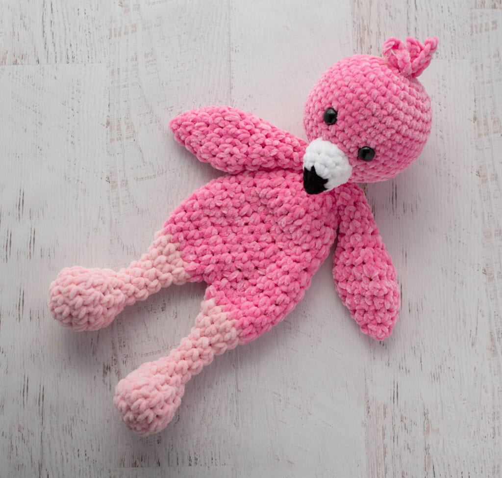 Crochet flamingo in pink yarn with a white and black beak on a whitewashed background