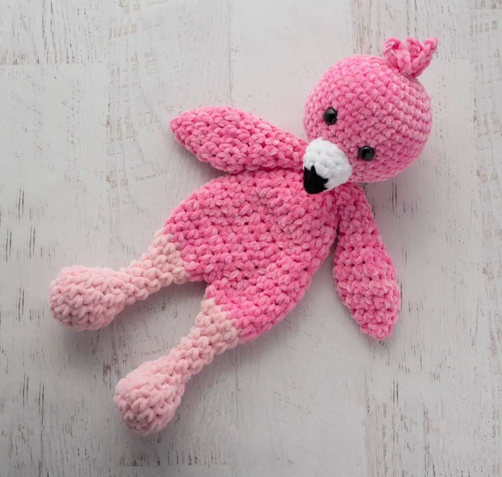 Crochet flamingo in pink yarn with a white and black beak on a whitewashed background