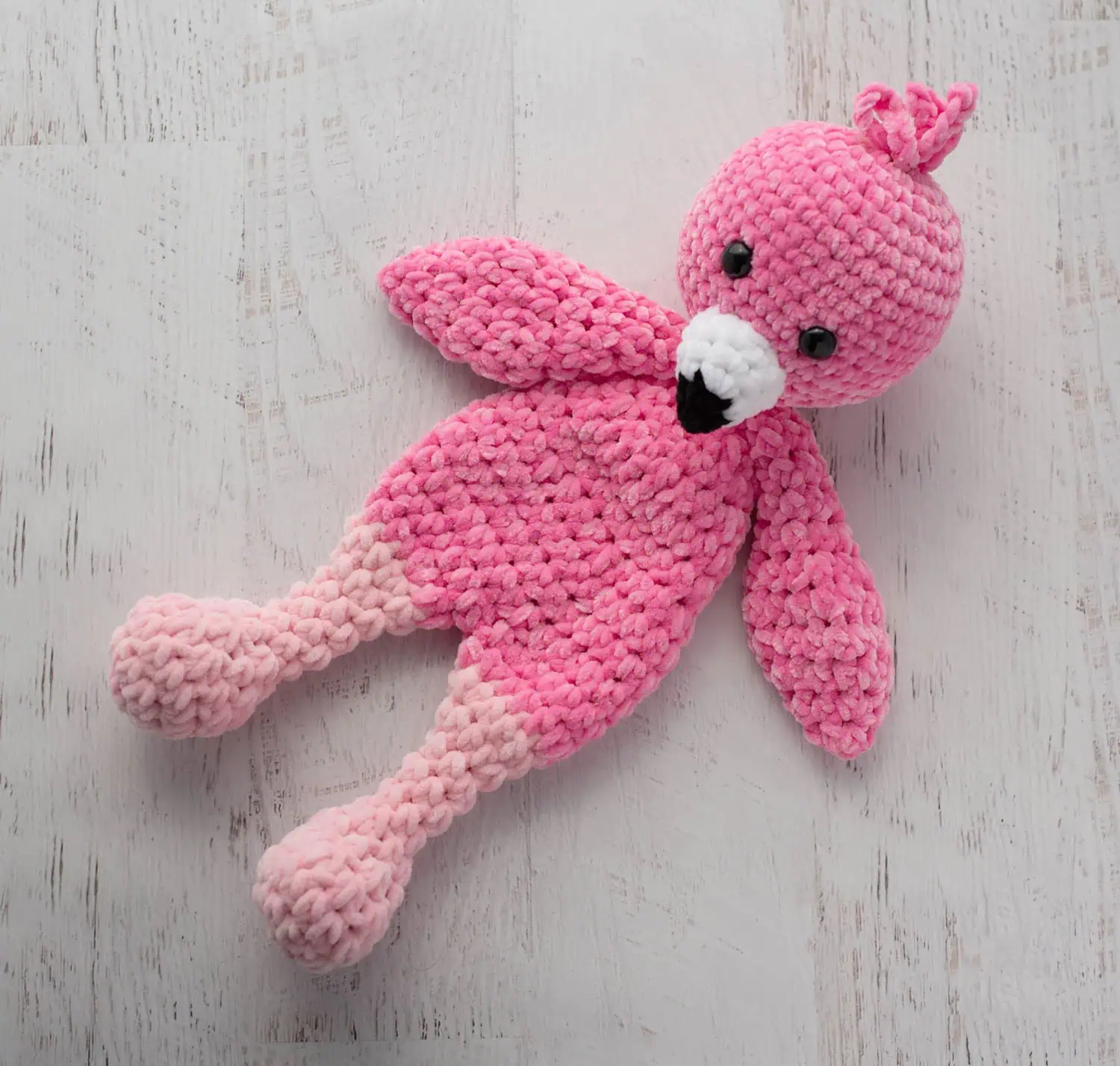 Crochet flamingo in pink yarn with a white and black beak on a whitewashed background