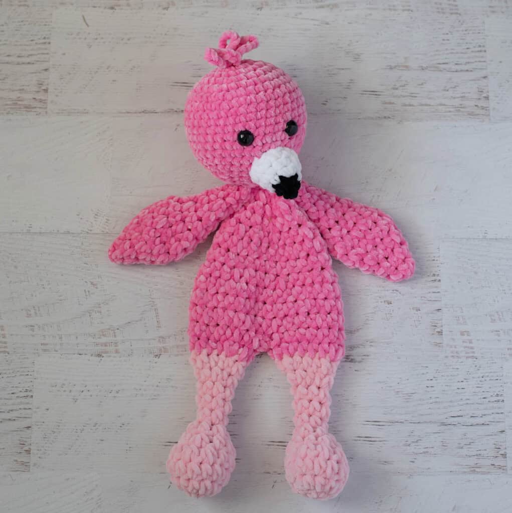 Crochet flamingo in pink yarn with a white and black beak on a whitewashed background