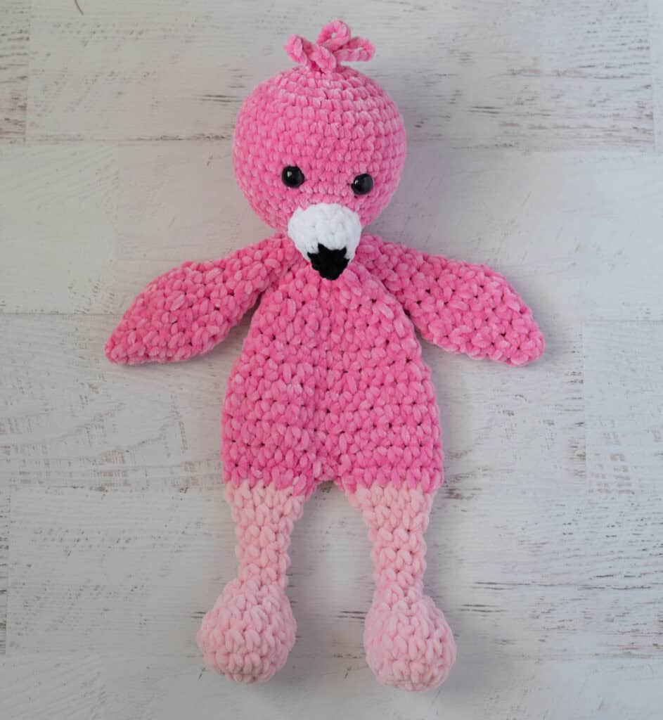 Crochet flamingo in pink yarn with a white and black beak on a whitewashed background