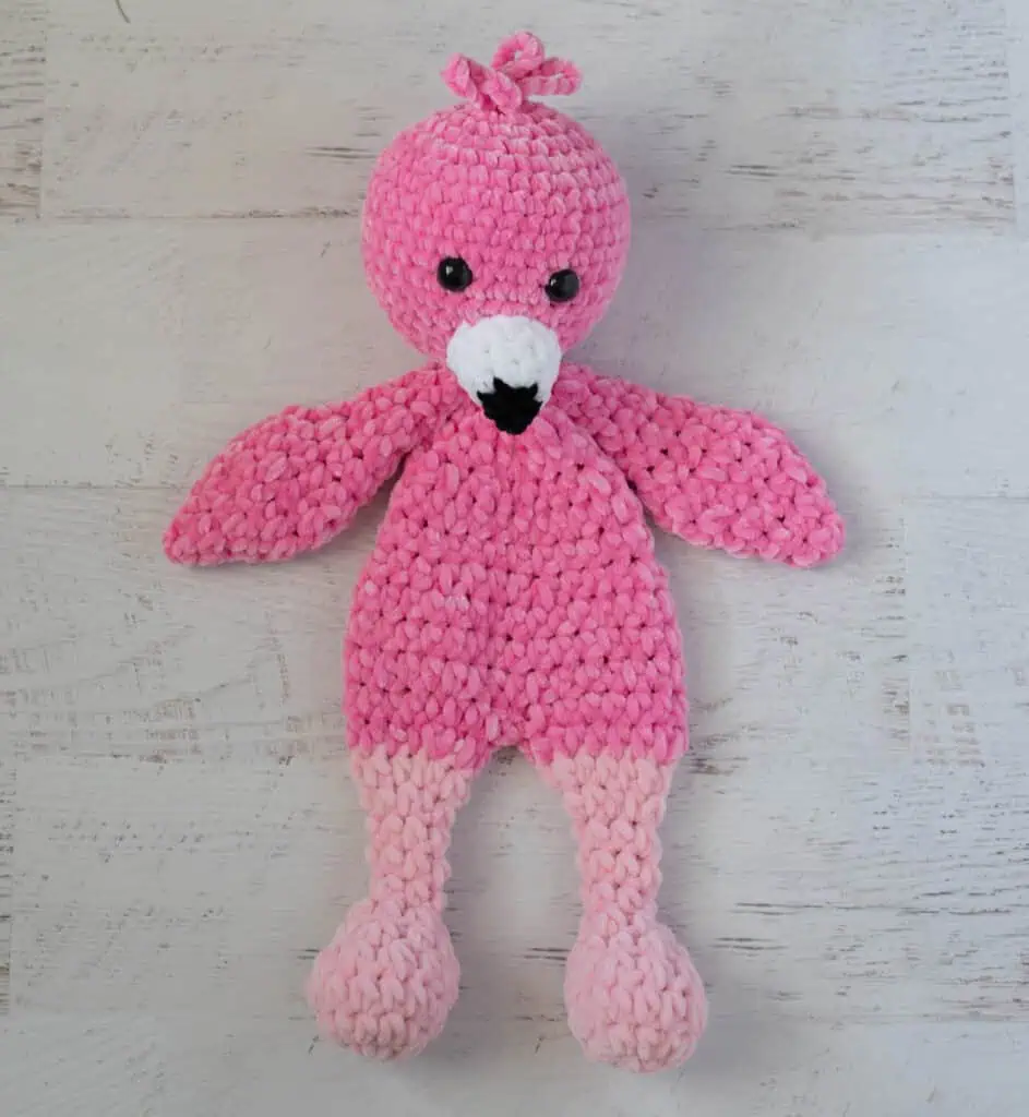 Crochet flamingo in pink yarn with a white and black beak on a whitewashed background