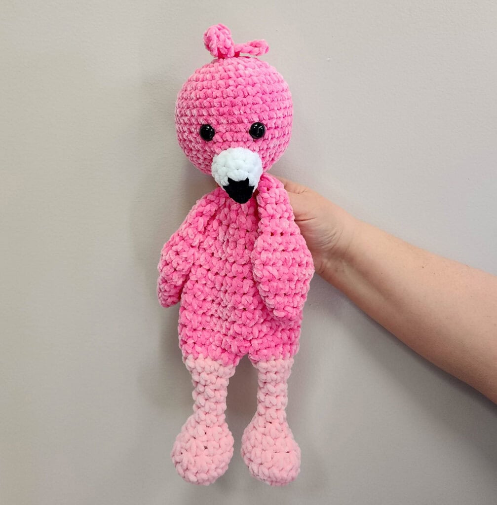 Crochet flamingo in pink yarn with a white and black beak on a whitewashed background