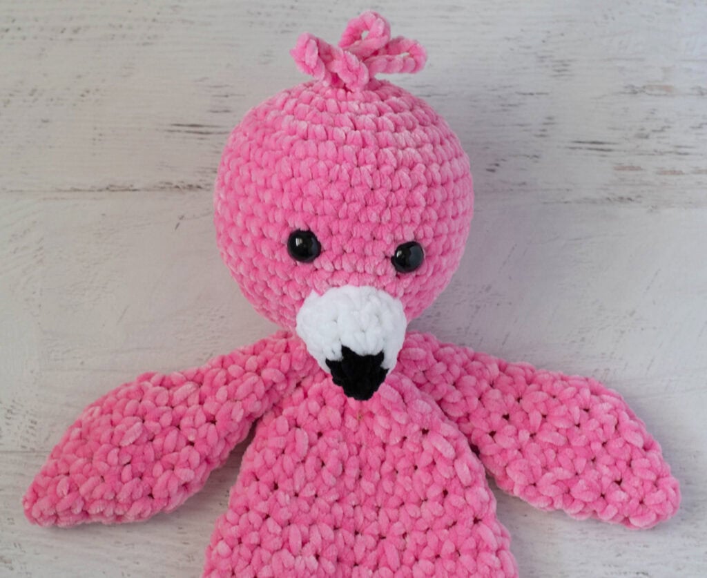 Crochet flamingo in pink yarn with a white and black beak on a whitewashed background