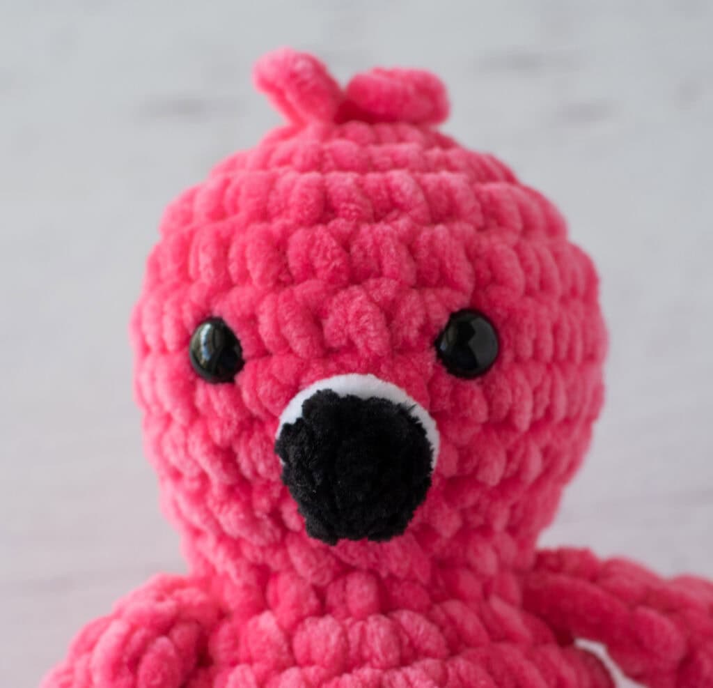 Hot pink crochet flamingo with a black beak close up view