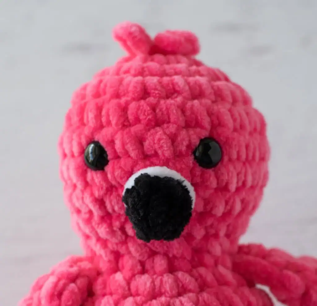 Hot pink crochet flamingo with a black beak close up view