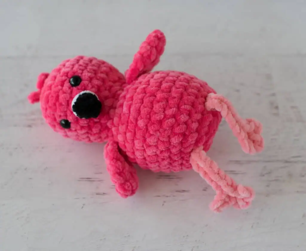 Hot pink crochet flamingo with a black beak and pink legs laying down