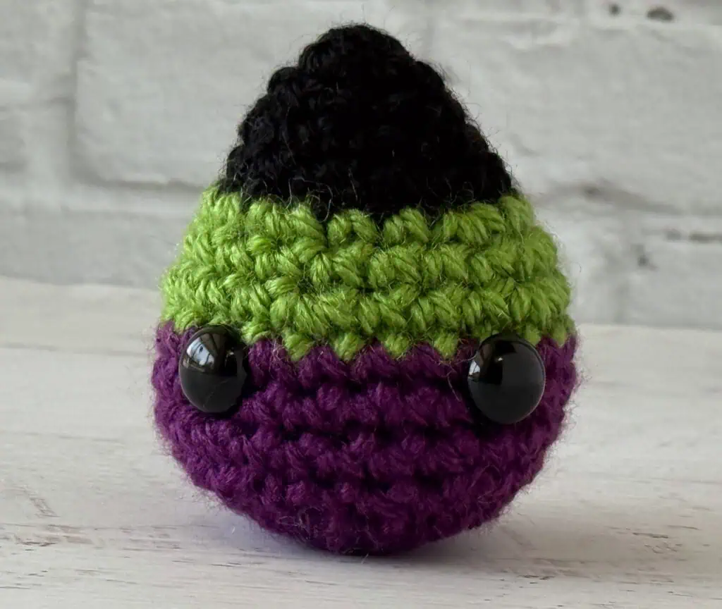 Black, green and purple crochet candy corn with eyes on a white washed table