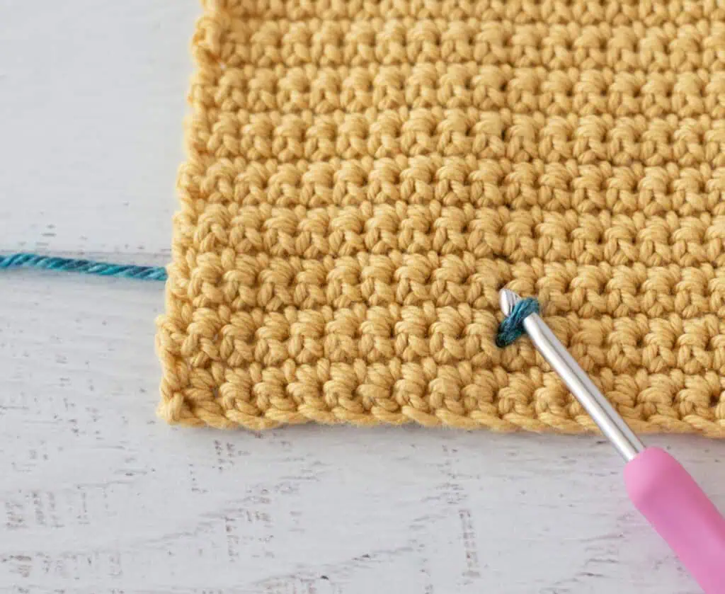 Yellow single crochet swatch with a blue yarn stitch and a pink crochet hook