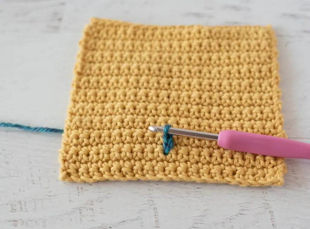 Yellow single crochet swatch with a blue yarn stitch and a pink crochet hook