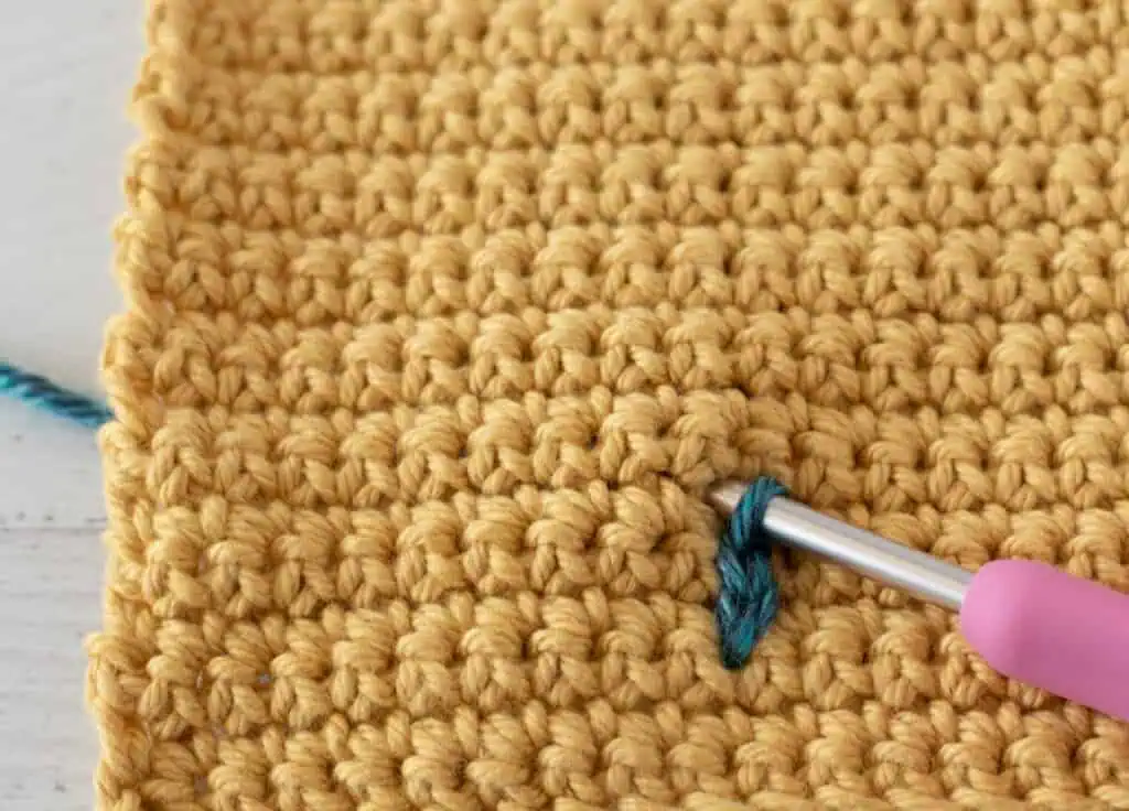 Yellow single crochet swatch with a blue yarn stitch and a pink crochet hook
