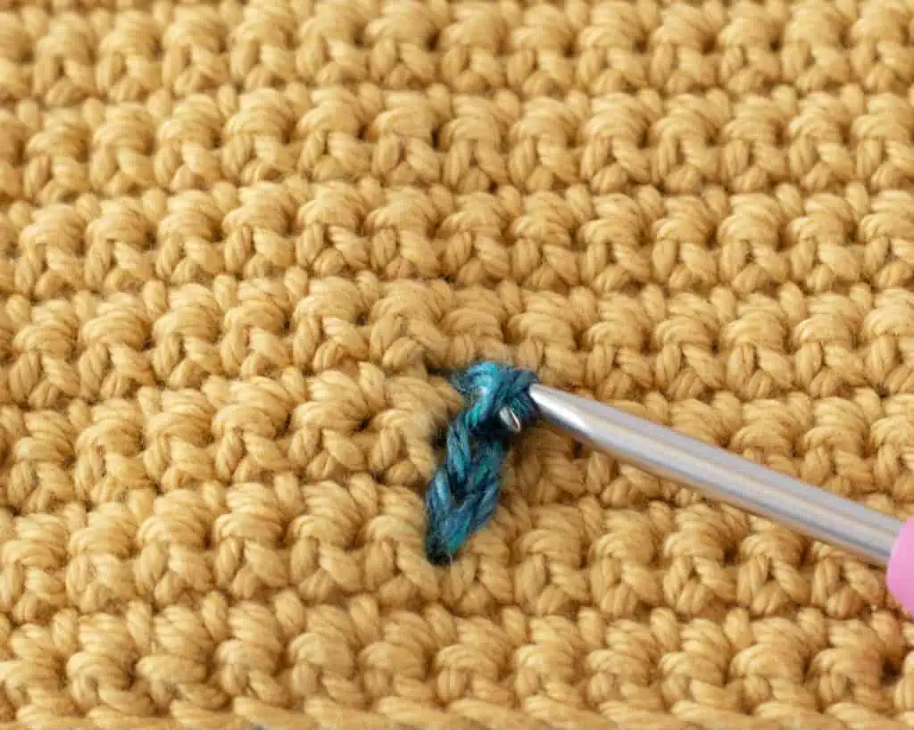 Yellow single crochet swatch with a blue yarn stitch and a pink crochet hook