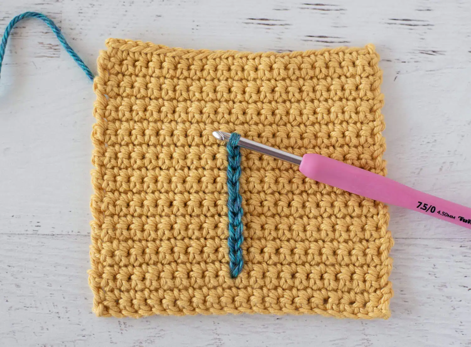 Yellow single crochet swatch with a blue yarn stitch and a pink crochet hook