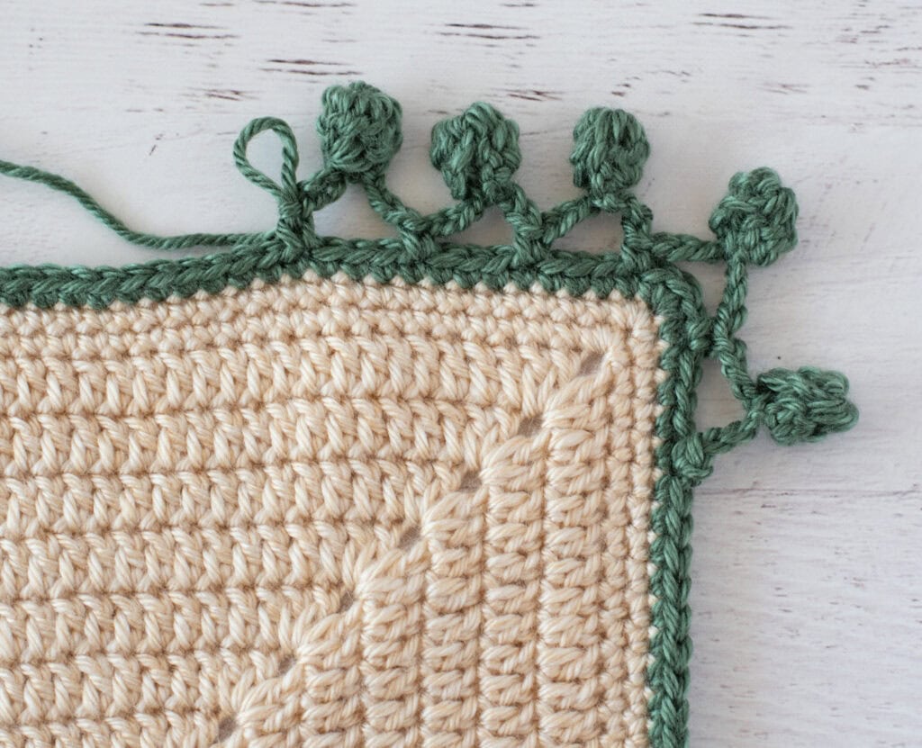 Step by step photo of crochet pom pom border in green yarn on an ivory blanket