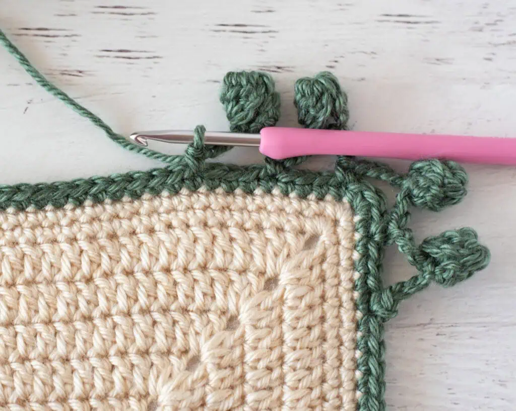 Step by step photo of crochet pom pom border in green yarn on an ivory blanket